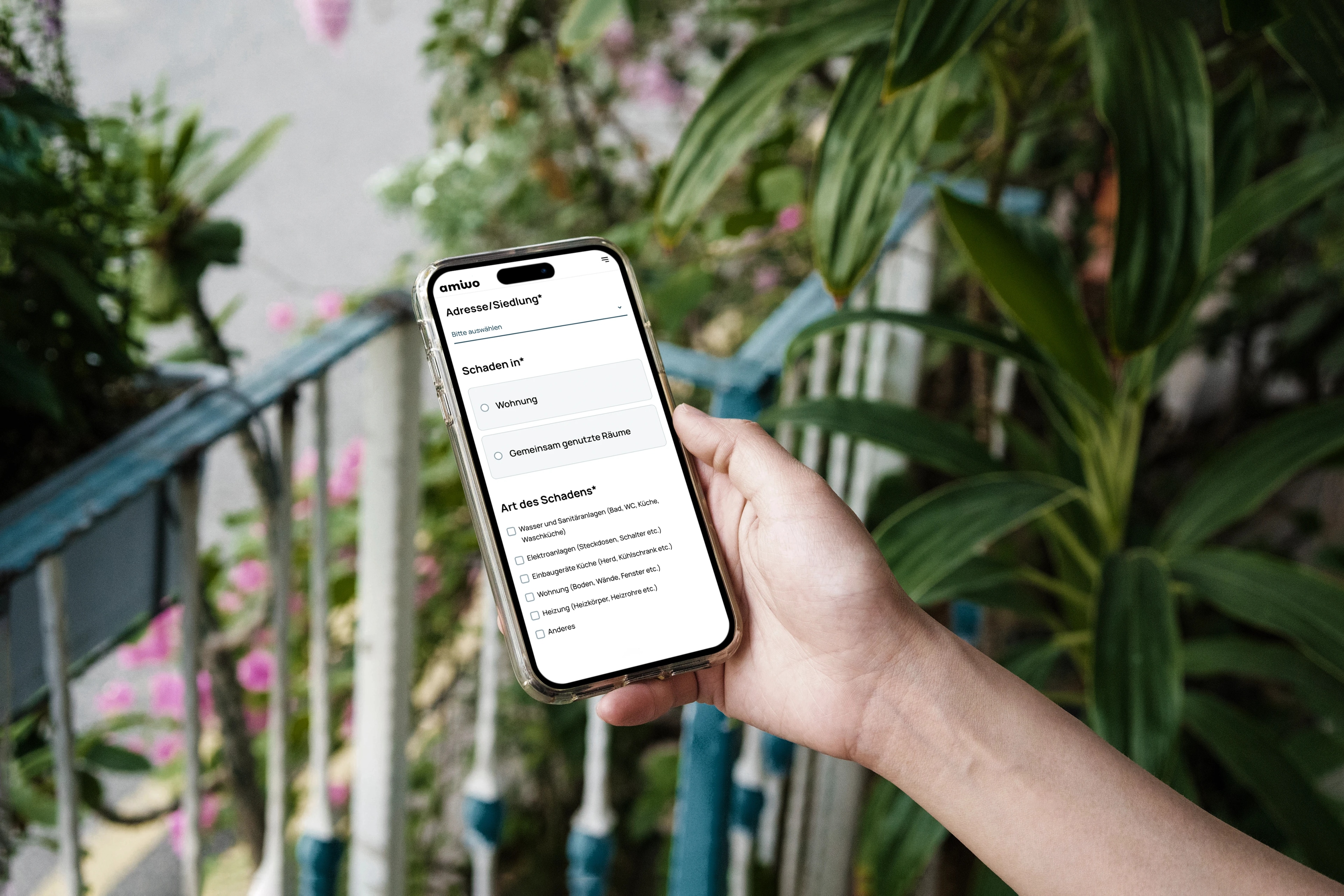 Hand hält modernes iPhone, darauf ist die Webapplikation amiwo zu sehen - im Hintergrund Pflanzen auf einem mediterranen Balkon.