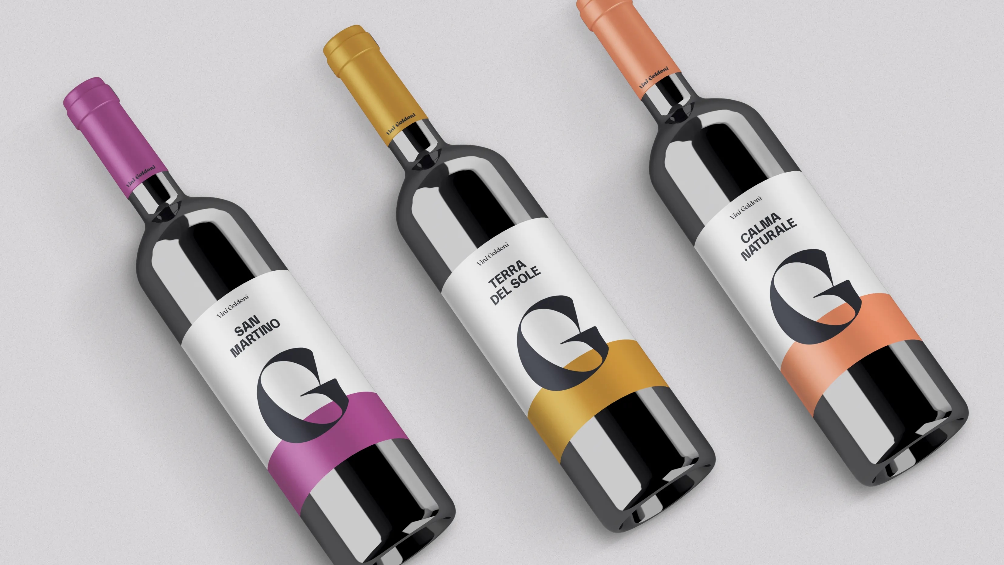 Das Bild zeigt drei Weinflaschen von "Vini Goldoni" in einer diagonalen Anordnung. Jede Flasche hat ein modernes, minimalistisches Etikett und eine unterschiedliche Farbgestaltung für die Kapsel und den unteren Teil des Etiketts.