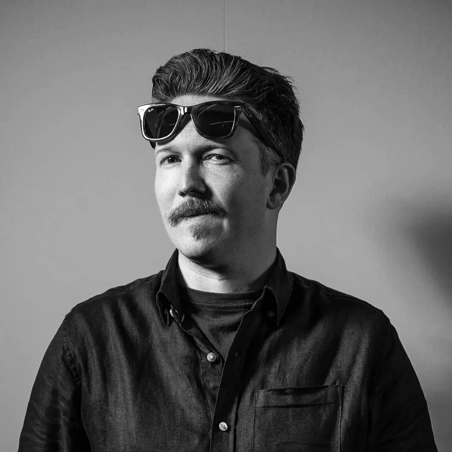 Severin Glaser schaut verschmitzt in die Kamera, hat eine Sonnenbrille auf der Stirn, monochrome Farbwelt.